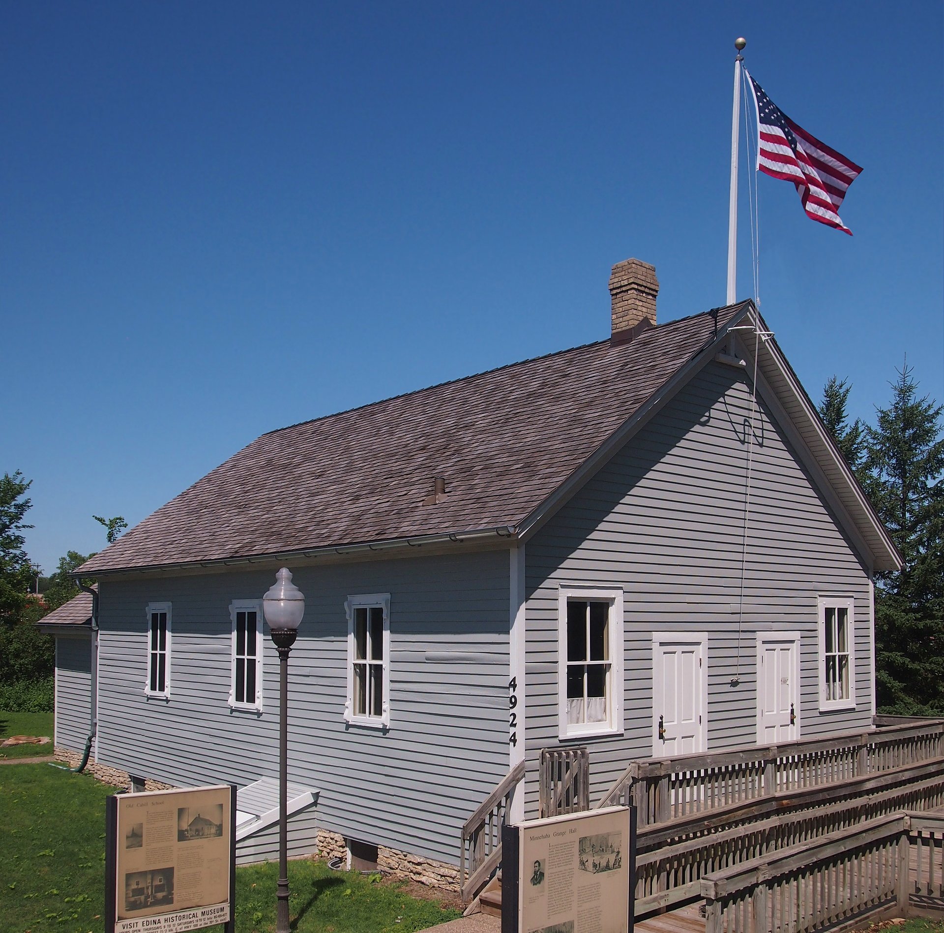 Gray wooden schoolhouse with white trim, an accessible ramp and a flagpole.