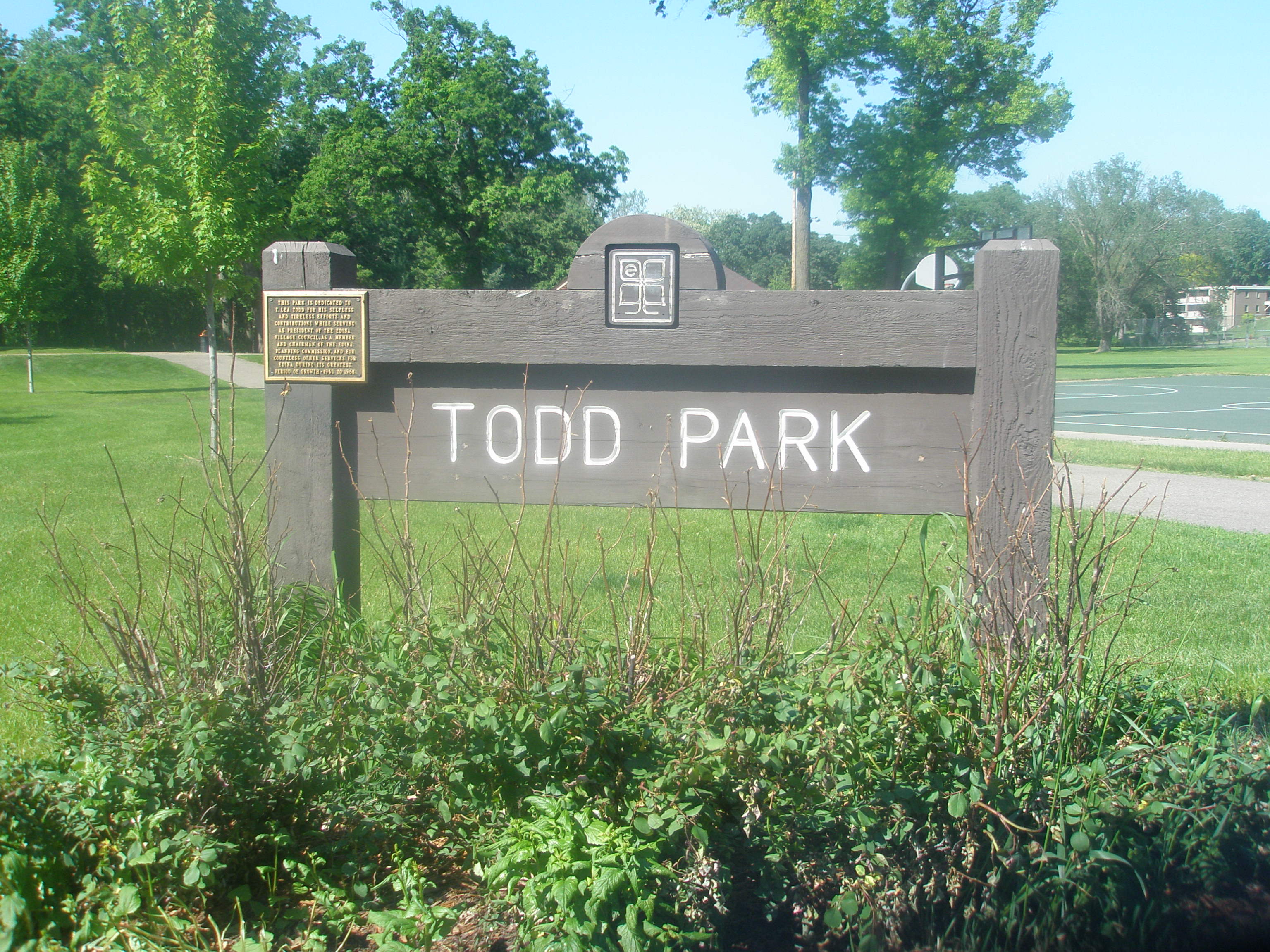 Wooden Todd Park sign in front of a green lawn and basketball court.