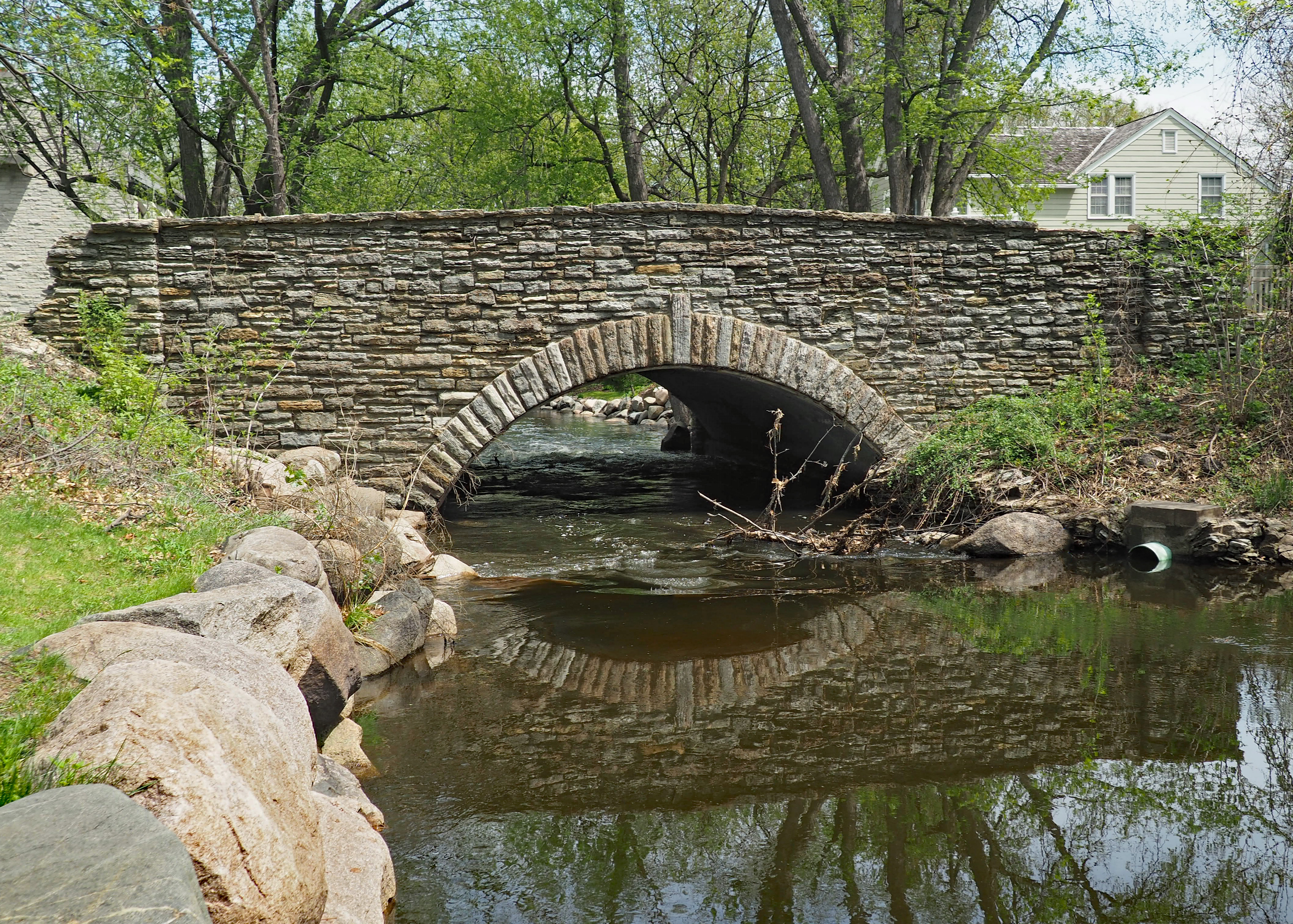 Stone arch bridge spanning Minnehaha Creek, with trees and rocks along the banks.